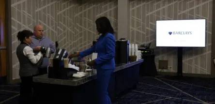 Black women in a blue suit at a refreshment table next to a screen that says Barclays.
