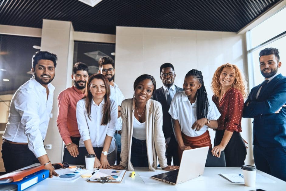 A diverse group of young people in an office setting standing around a table. 