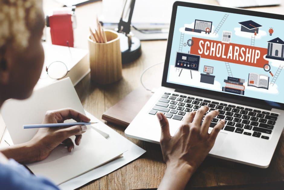 Women sitting at laptop with the word scholarship and related imagery on the screen. 