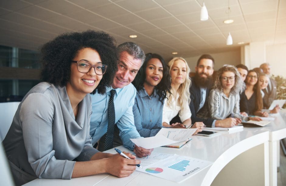 Un grupo diverso de sonrientes profesionales de los negocios sentados a una mesa blanca. 