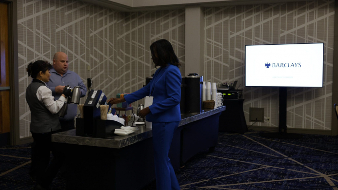 53742424959_120e594589_k Black women in a blue suit at a refreshment table next to a screen that says Barclays.