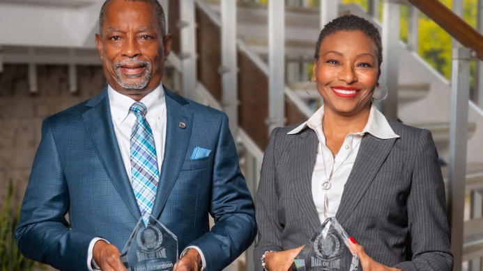Picture of Black man and woman in professional attire holding glass awards with stairs in the background.